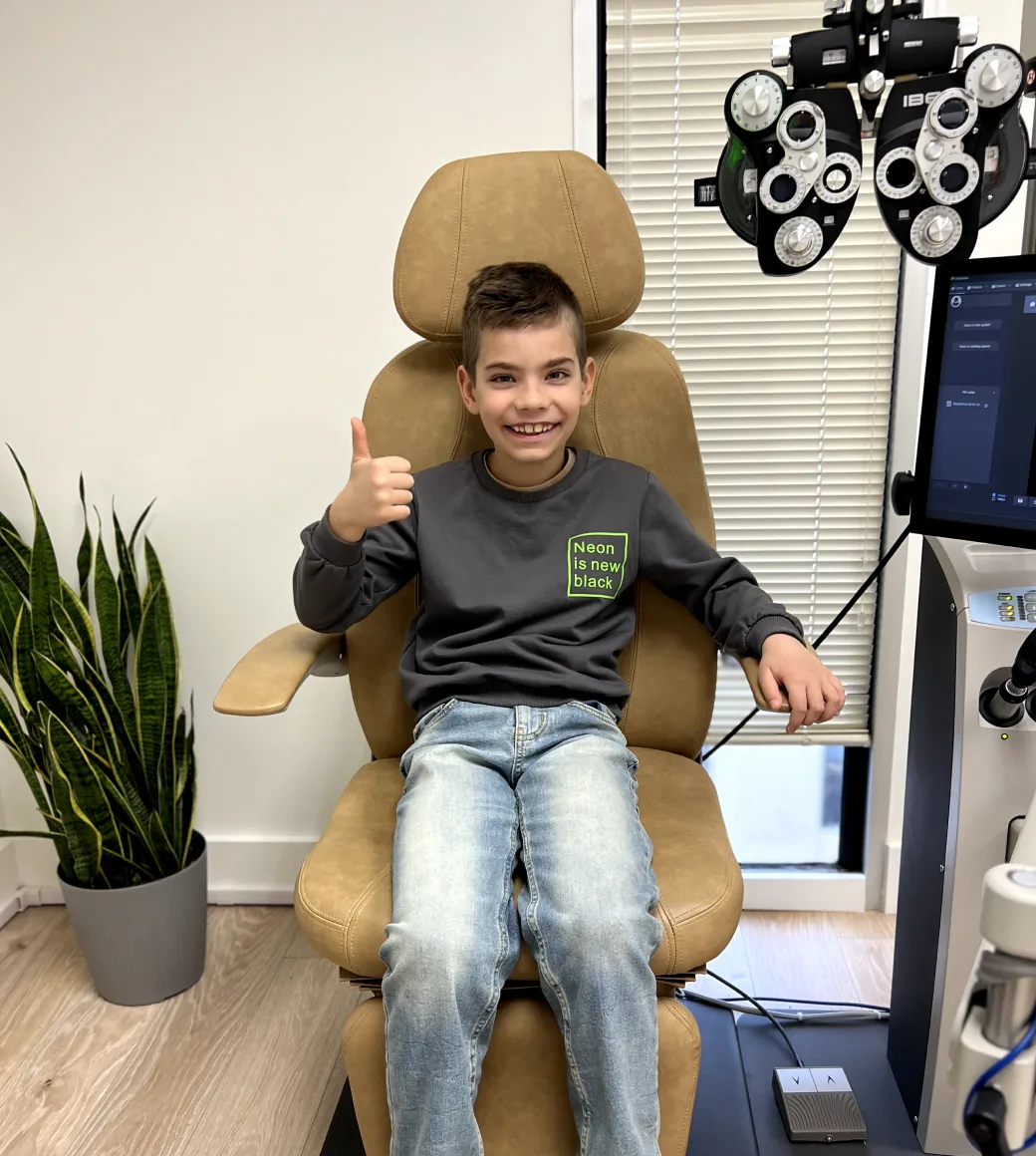 Young patient smiling and giving a thumbs up in optometry chair